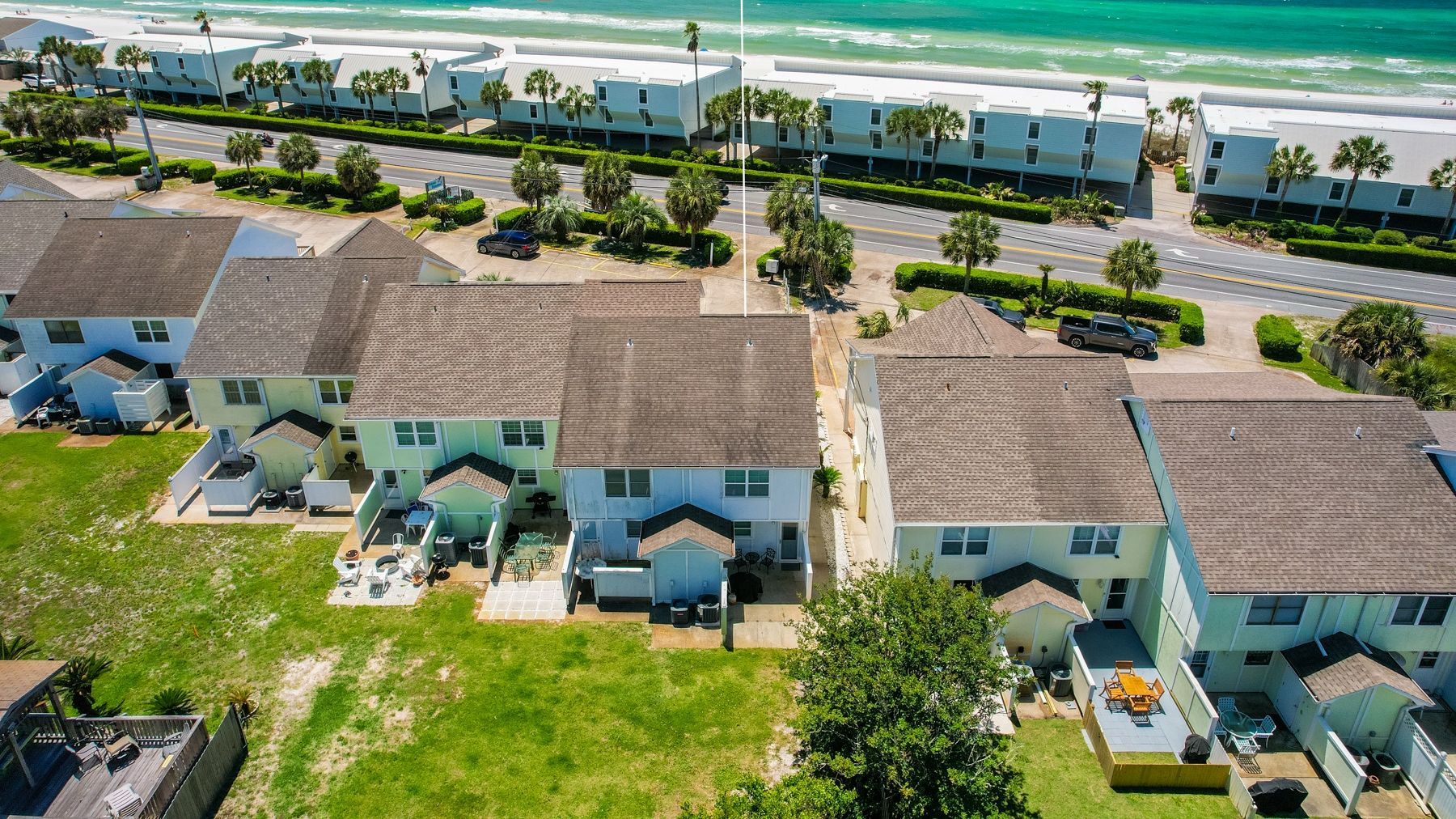 Una zona residenziale sulla costa, con diverse case a due piani, ognuna dotata di un giardino antistante e vista sulla spiaggia.
