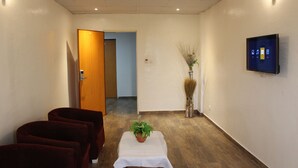 Un vestíbulo de hotel con un mostrador de recepción, una pantalla de televisión, una planta sobre una mesa y piso de madera.
