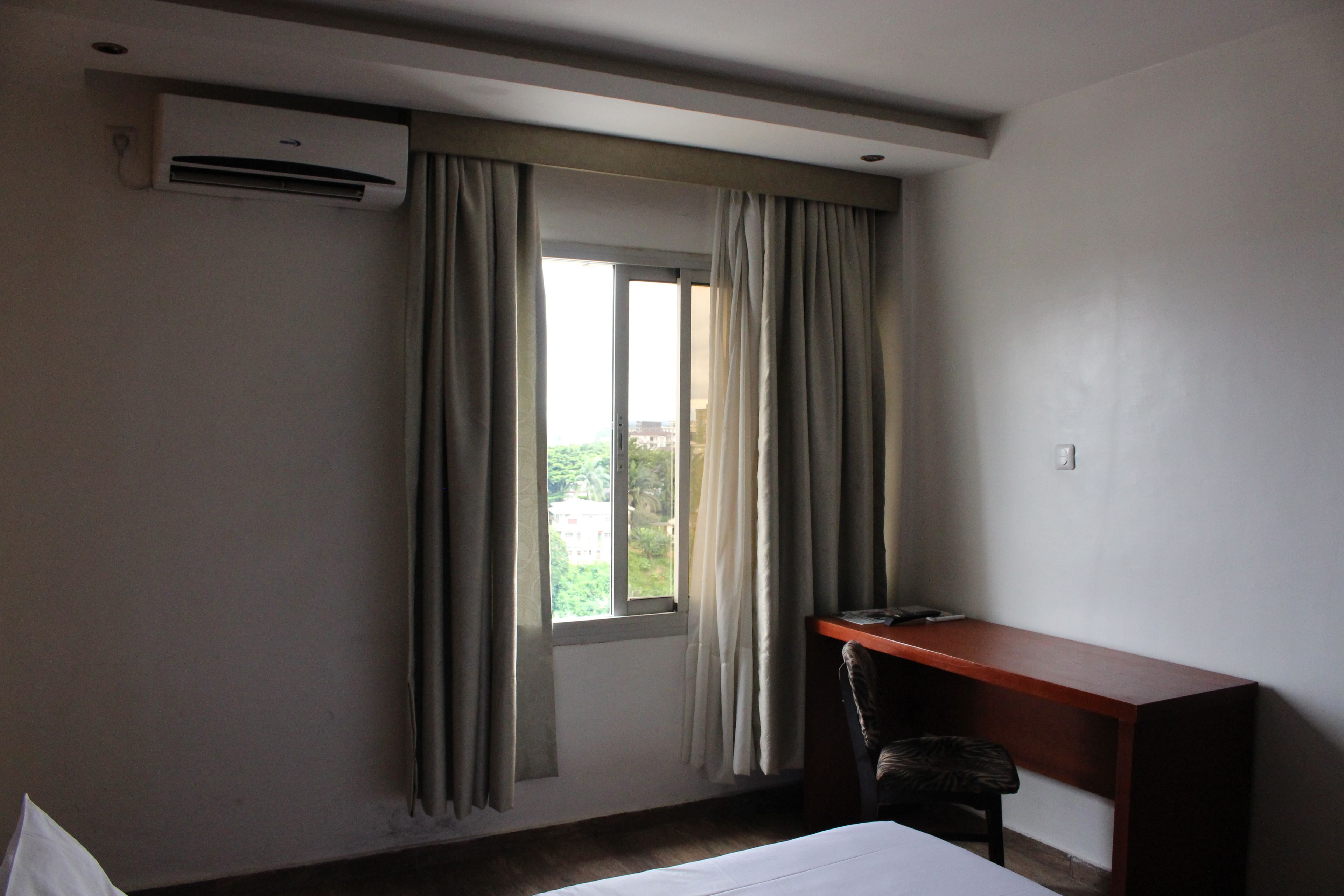 A hotel room with a bed, a desk, and a window with curtains.