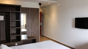 Habitación de hotel con cama, televisión montada en la pared, armario y espejo.