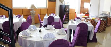 Un comedor con mesas redondas, sillas moradas y manteles blancos.