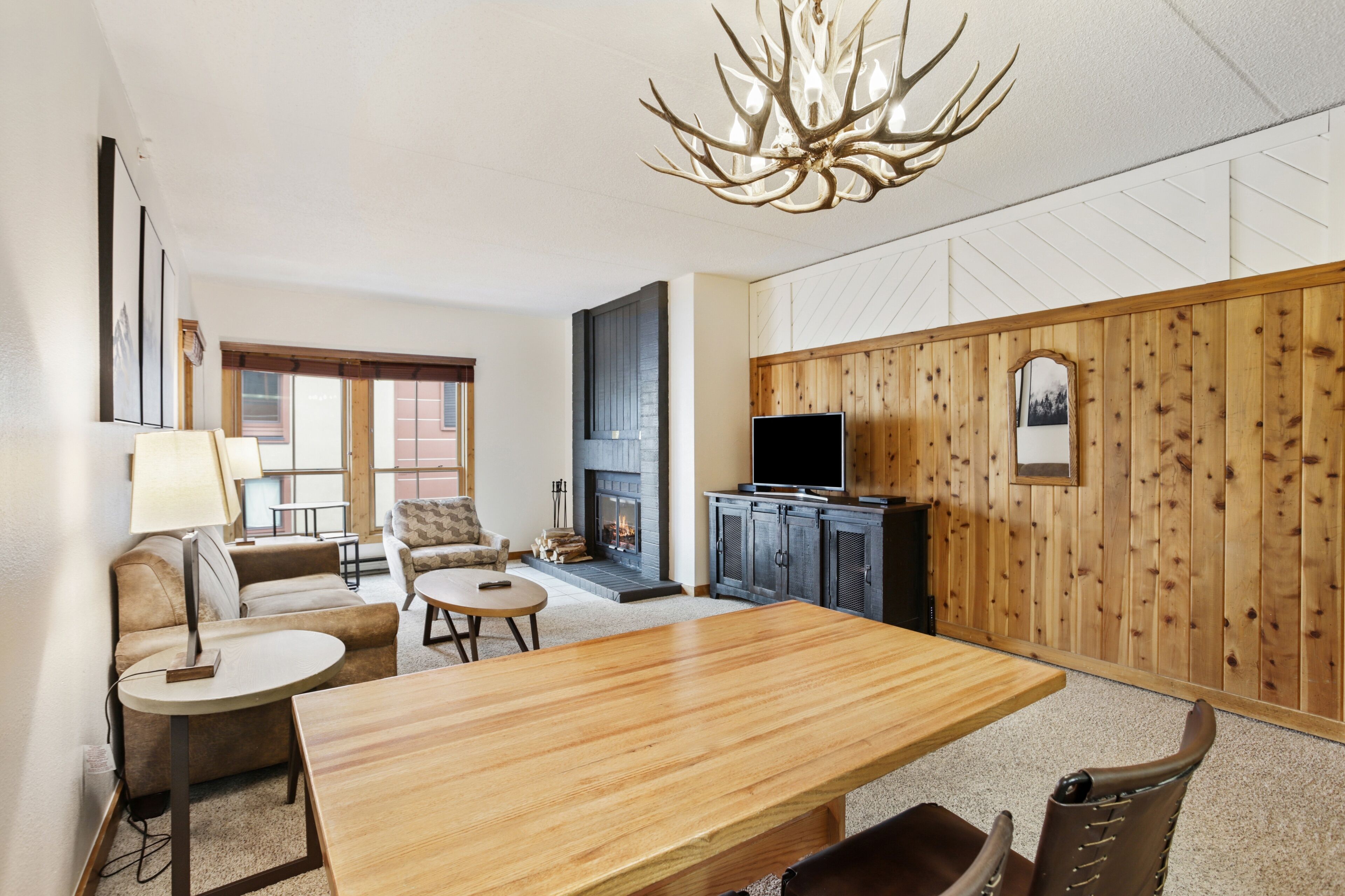 Een woonkamer met een houten eettafel, een open haard, een televisie en een grote kroonluchter.