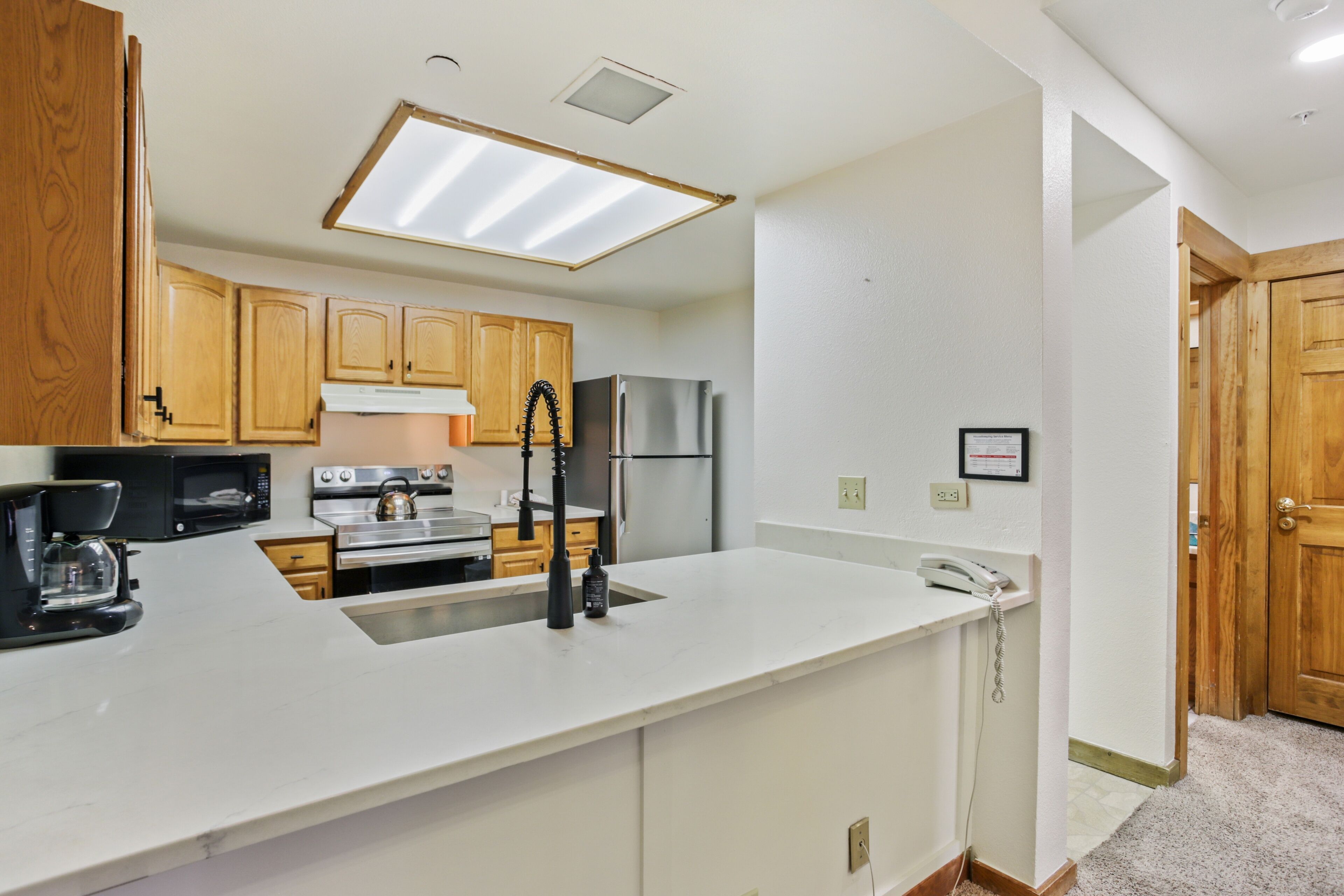 A kitchen with wooden cabinets, stainless steel appliances, a white countertop, and a skylight.