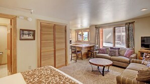 A living room with a sofa, a coffee table, a dining table with chairs, a TV, and a window with curtains. - Stay Slopeside At Peak 9, Cozy Studio Steps To Apres& Dining Studio Bedroom Condo by RedAwning (Breckenridge)