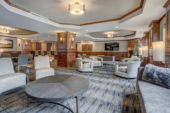 A spacious lobby with a large round table, several sofas, and armchairs. There is a wooden cabinet and a Christmas tree.