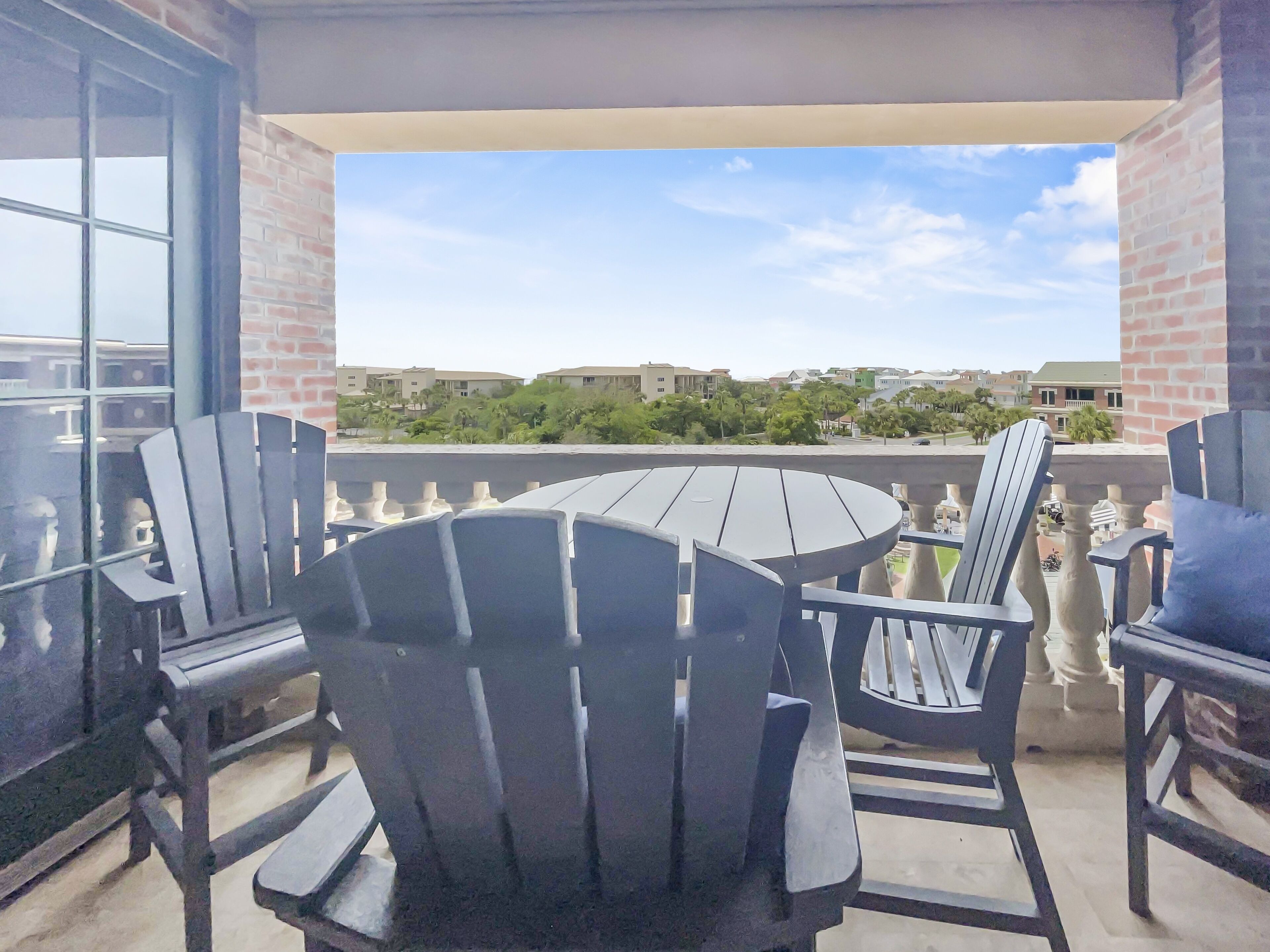 A balcony with a round table and four Adirondack chairs.