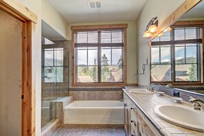 A bathroom with a bathtub, two sinks, and large windows with a view of trees and buildings. - Soaring Ceilings + Mins To Gondola/apres-ski - 2br Sleeps 6 2 Bedroom Townhouse by RedAwning (Breckenridge)