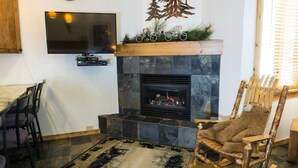A living room with a fireplace, a television mounted on the wall, and a dining area with chairs and a table. - Ski Trails 4058 (Truckee)
