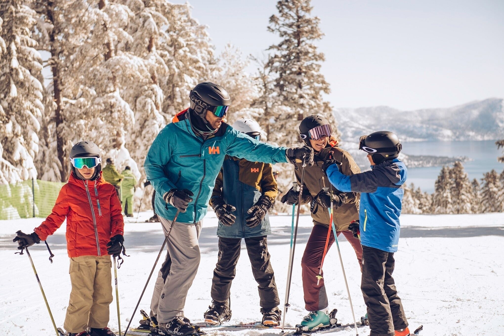 A group of skiers on a snowy slope with trees and mountains in the background.