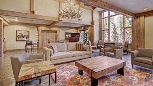 A spacious living room with a large chandelier, wooden beams, a sofa, armchairs, a coffee table, and a patterned rug. - Refined  With Sunny Views 2 Blocks To Downtown Breck 1 Bedroom Condo by RedAwning (Breckenridge)