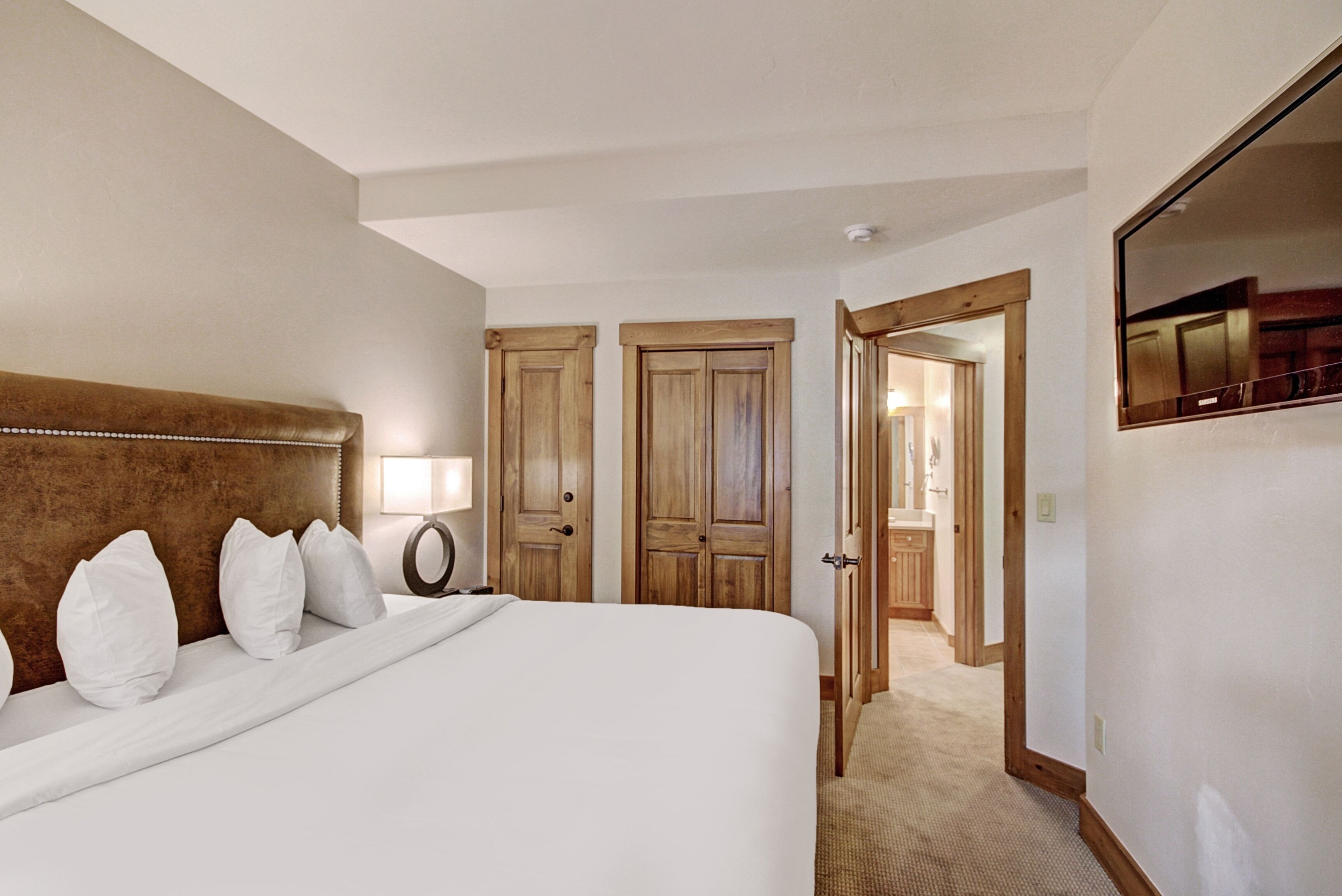 Una habitación de hotel con una cama grande, un armario de madera, un espejo y una puerta que da a un baño.
