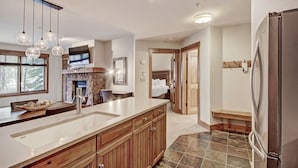 A modern kitchen with a large island, wooden cabinets, and a built-in oven. There is a dining area with a table and chairs, and a TV mounted on the wall. - Refined  With Sunny Views 2 Blocks To Downtown Breck 1 Bedroom Condo by RedAwning (Breckenridge)