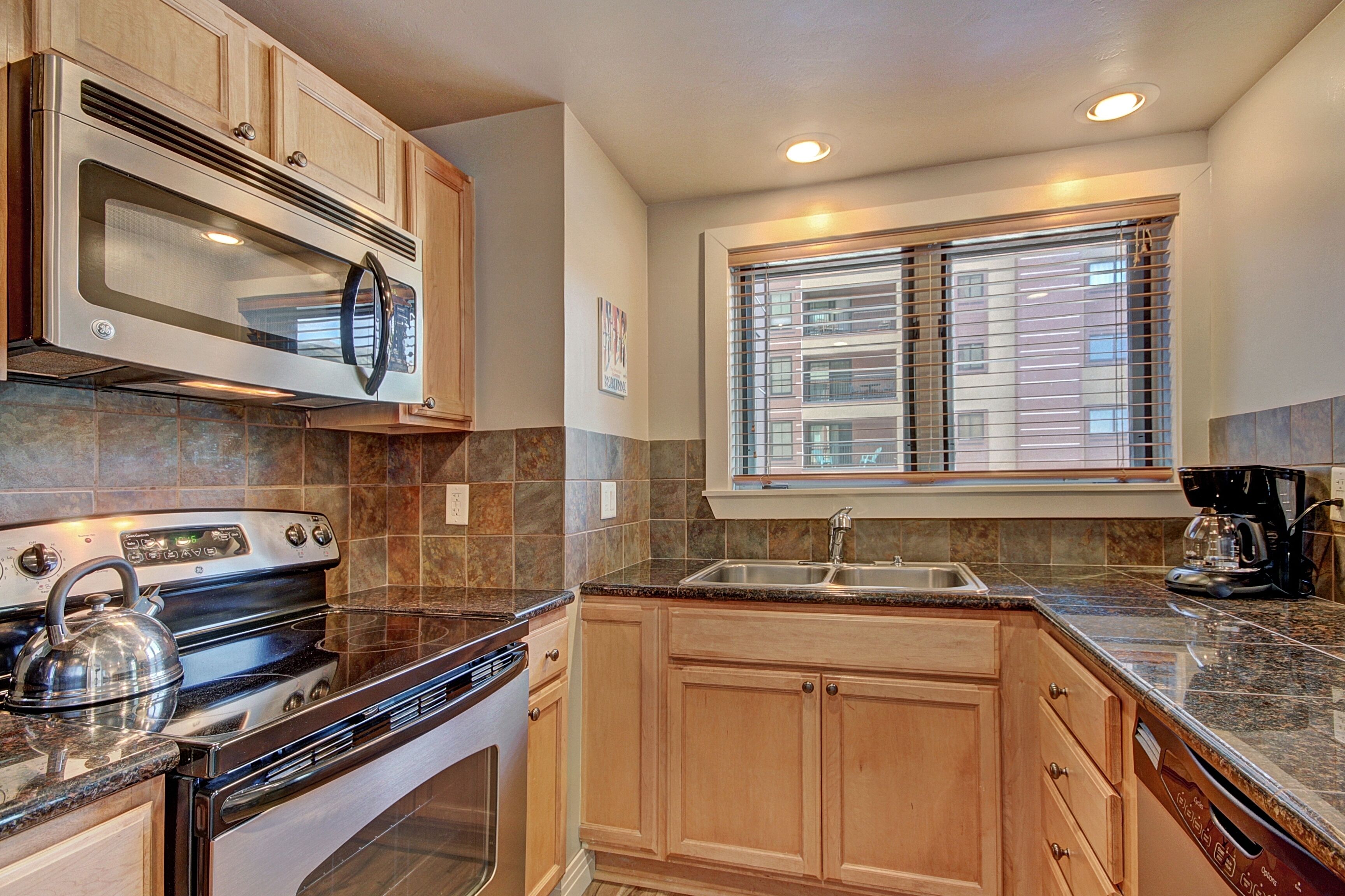 A kitchen with a microwave, stove, sink, and coffee maker.