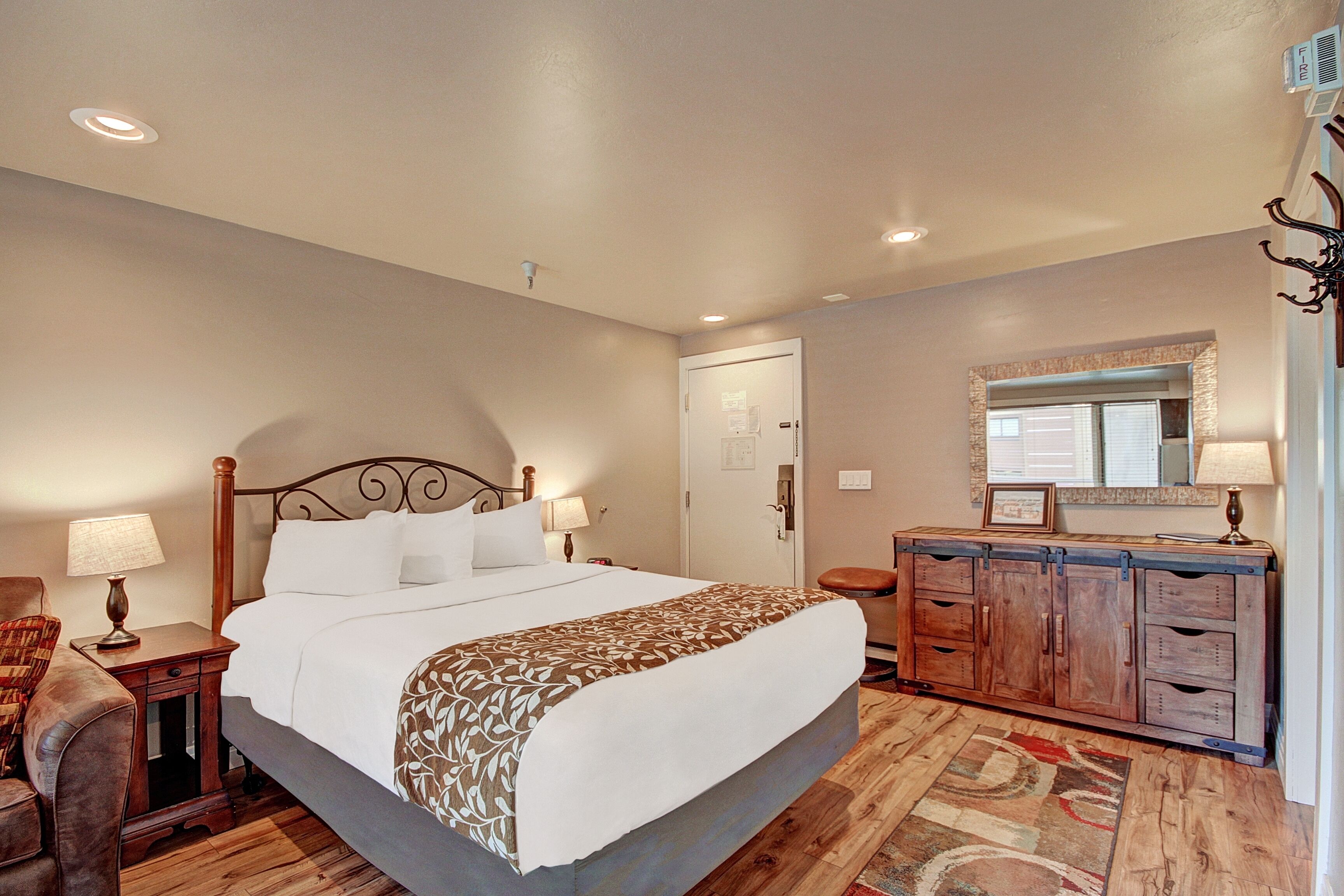 A hotel room with a large bed, a wooden dresser, a mirror, and a chair.