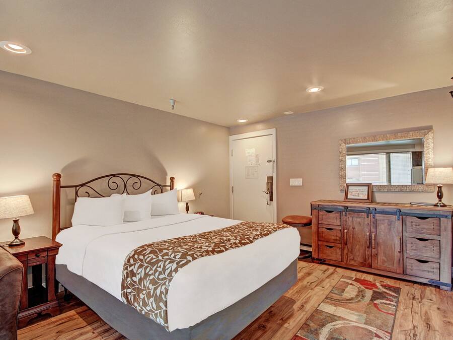 A hotel room with a large bed, a wooden dresser, a mirror, and a chair.