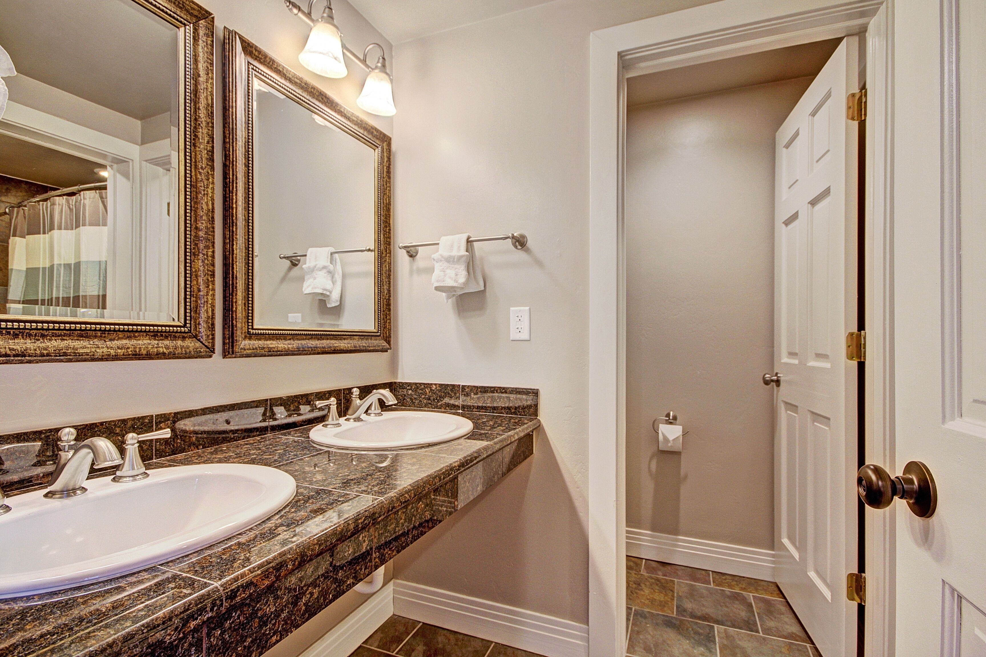 A bathroom with two sinks, a large mirror, and a door leading to another room.