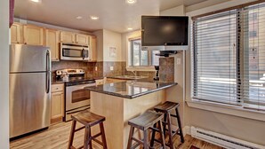 A modern kitchen with stainless steel appliances, wooden cabinets, and a large island with stools. - Winter Ski-in/out Studio Sleeps 4, Steps To Historic Main St Studio Bedroom Condo by RedAwning (Breckenridge)