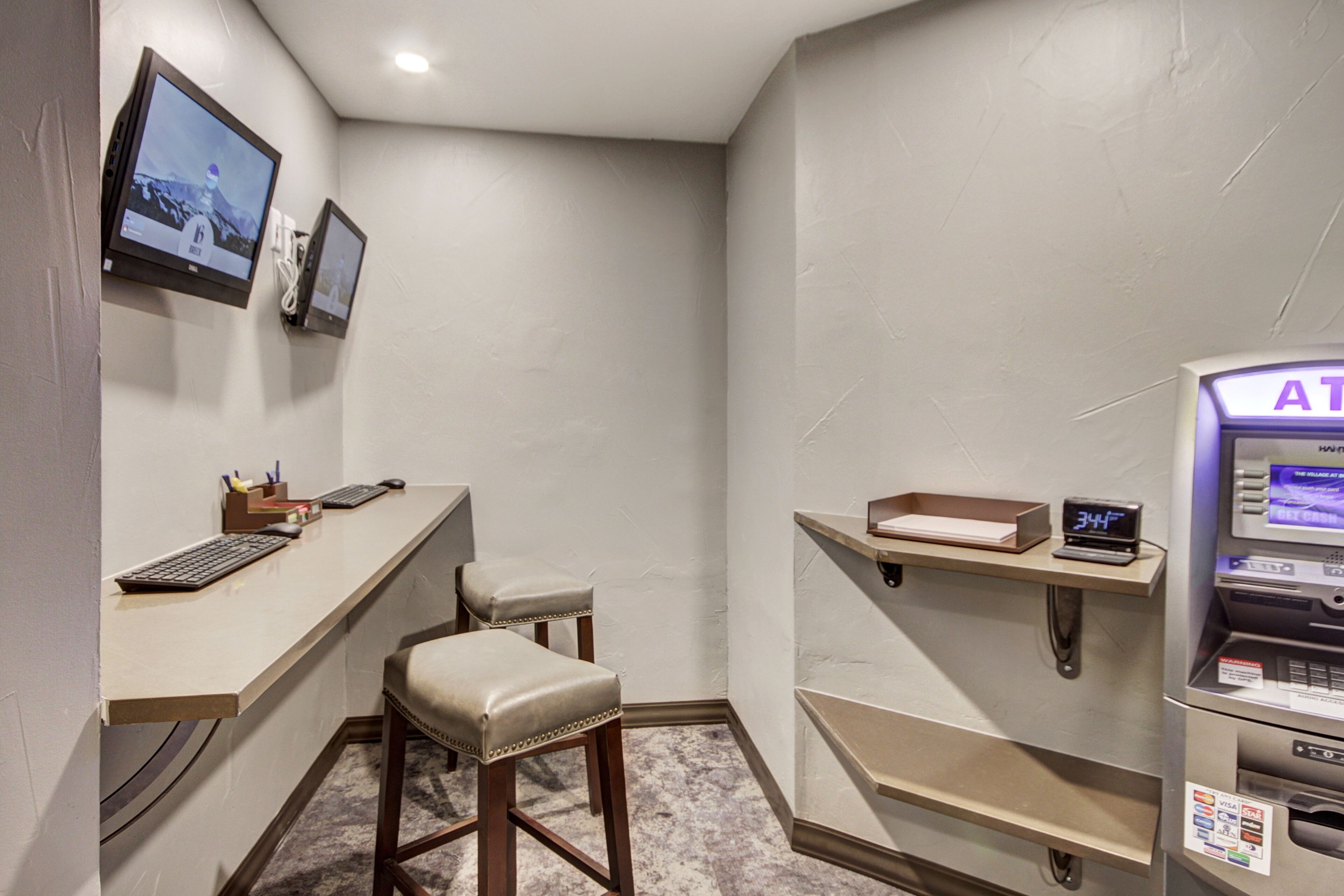 A small, private room with a desk, two chairs, a computer, and an ATM.