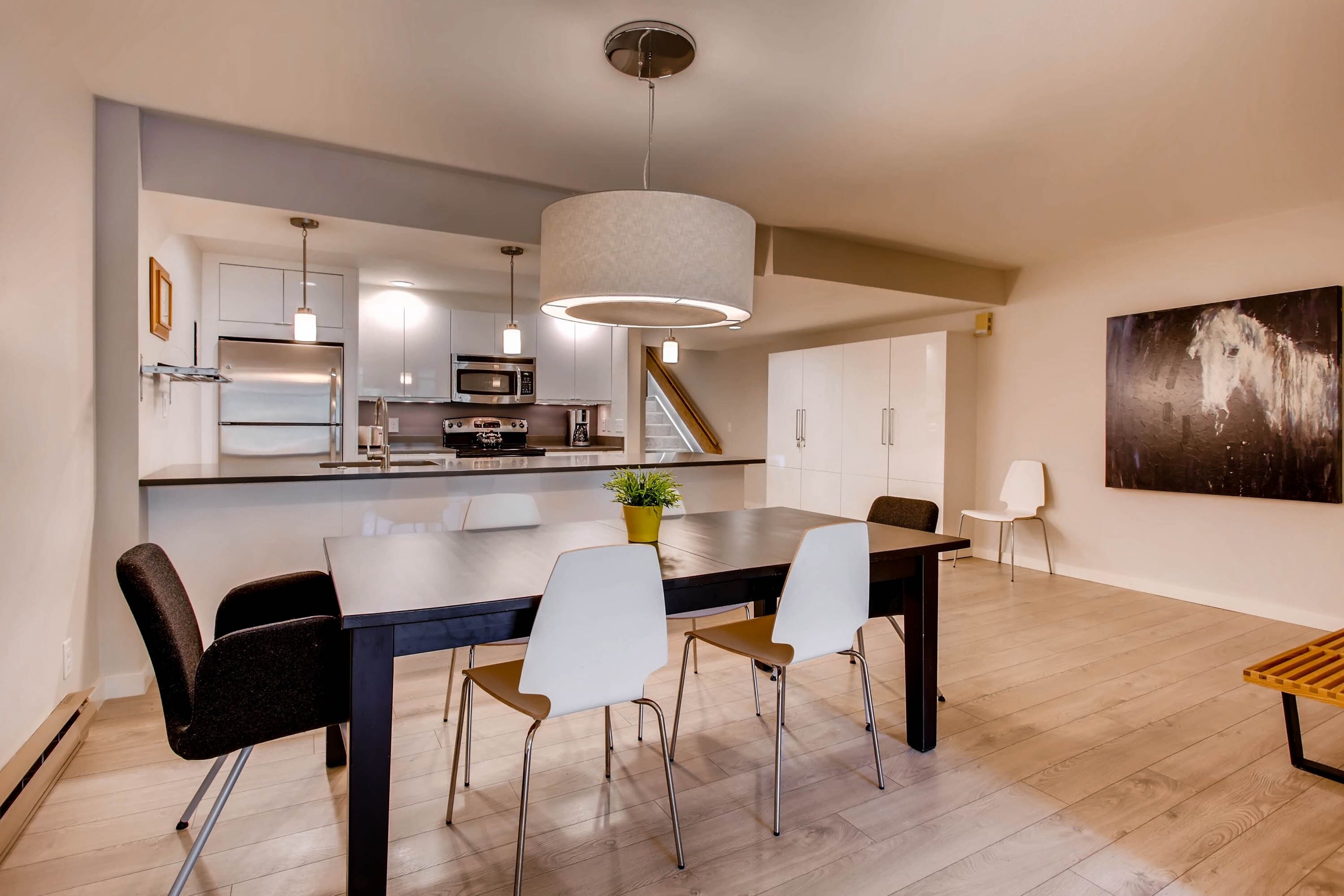 A modern kitchen with stainless steel appliances, a dining area with a large table and chairs, and a staircase leading to another level.