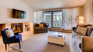 A modern living room with a sofa, armchair, and coffee table, a fireplace, and a large window with curtains. - Sts. Johns 2507 (Keystone)