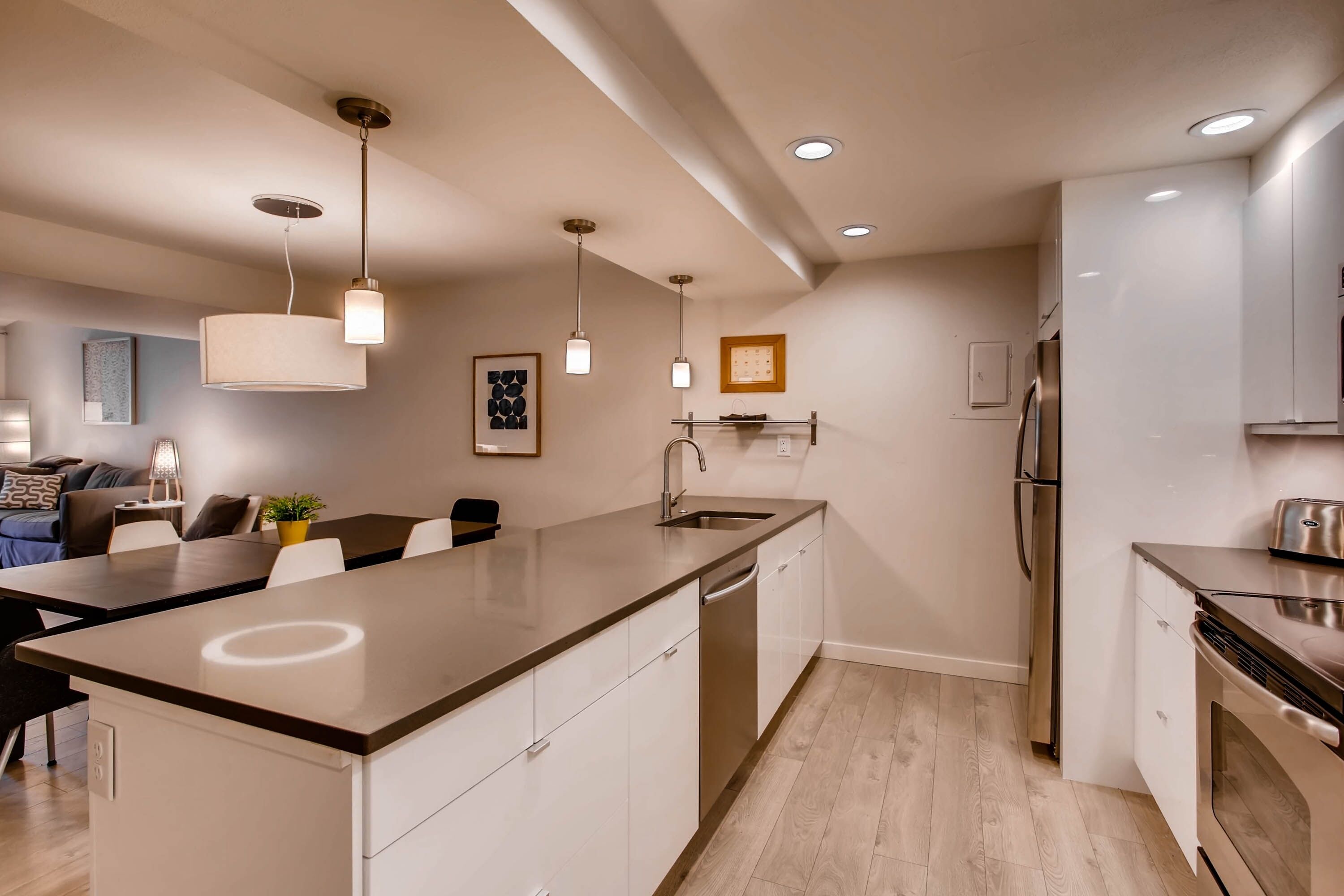A modern kitchen with a central island, stainless steel appliances, pendant lighting, and a dining area with a sofa and table.