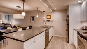 A modern kitchen with a central island, stainless steel appliances, pendant lighting, and a dining area with a sofa and table. - Sts. Johns 2507 (Keystone)