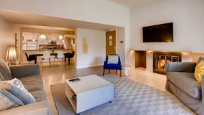 A modern living room with a sofa, a coffee table, and a TV. There is a kitchen in the background with a dining area. - Sts. Johns 2507 (Keystone)