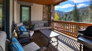 A wooden deck with outdoor furniture, a stone wall, and a view of mountains. - Ski-in/ Ski-out 3br 3.5ba Forest + Mountain Views Sleeps 8 3 Bedroom Condo by RedAwning (Avon)