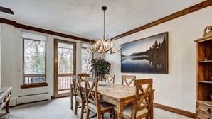 A dining room with a wooden table and chairs, a chandelier, a painting of a lake, and a wooden bookshelf. - Elkhorn 408 (Avon)