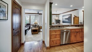 A spacious kitchen with wooden cabinets and a dishwasher, a dining area with a table and chairs, and a view of the outdoors through a large window. - Elkhorn 408 (Avon)
