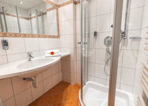 Un baño moderno con lavamanos, espejo y ducha blancos.