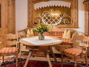 A wooden dining table with a lace tablecloth, surrounded by wooden chairs with plaid cushions. A vase with flowers is placed on the table.