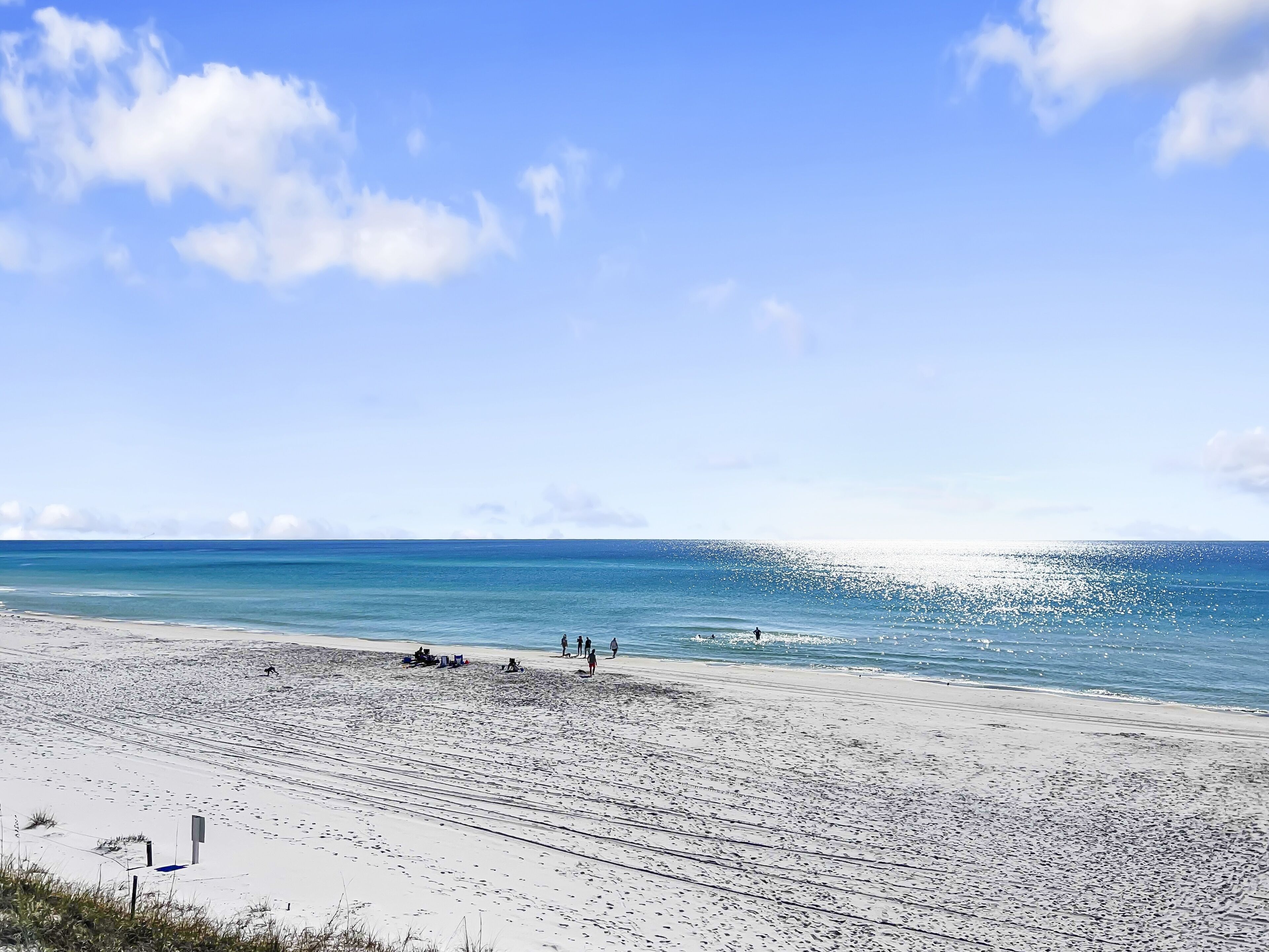 A beach with a clear sky, calm sea, and footprints leading to the water.
