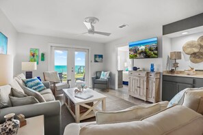 A spacious living area with a sofa, armchairs, a coffee table, and a TV. There is a view of the ocean through a glass door. - Sunseekers - 2 - 2 Br condo by RedAwning (Santa Rosa Beach)