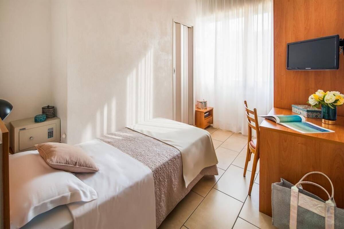 Une chambre d’hôtel comprenant un lit, une table de chevet, un bureau, une chaise, une télévision et une fenêtre avec des rideaux.