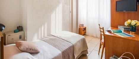 Habitación de hotel con cama, mesita de noche, escritorio, silla, televisor y ventana con cortinas.