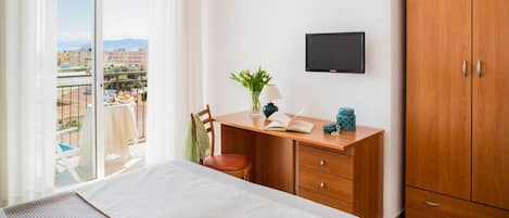 A bedroom with a bed, a desk, a chair, a TV, and a wardrobe.