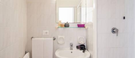 A bathroom with white tiles, a sink, a mirror, a towel rack, and a shower.
