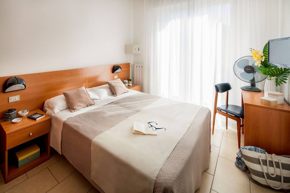 Une chambre d’hôtel bien rangée, avec un lit, des tables de chevet, un bureau et une chaise.