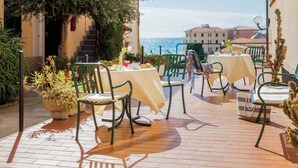 An outdoor patio with tables and chairs, a potted plant, and a view of the sea. - Hotel Europa (Finale Ligure)