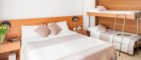 A hotel room with a large bed, a smaller bed on a loft, a bedside table with a lamp, a nightstand, and a vase with flowers.