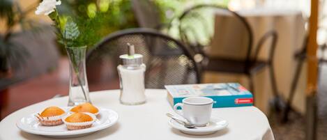 A table with a white tablecloth, a white cup with a saucer, a book, and three muffins on a plate.