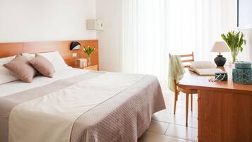 Une chambre d’hôtel avec un lit bien fait, un bureau en bois avec une lampe, une chaise et une petite table sur laquelle est posé un vase de fleurs.