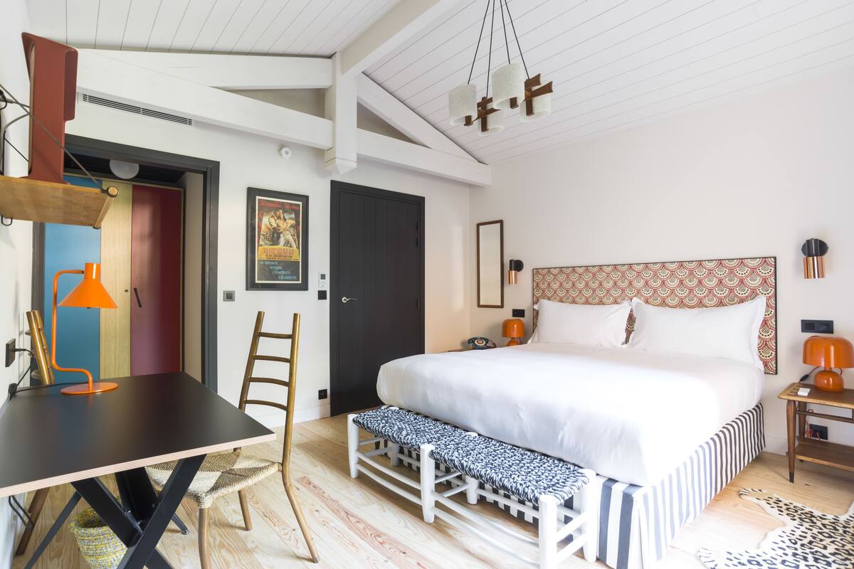 A modern bedroom with a large bed, a desk, and a bench.