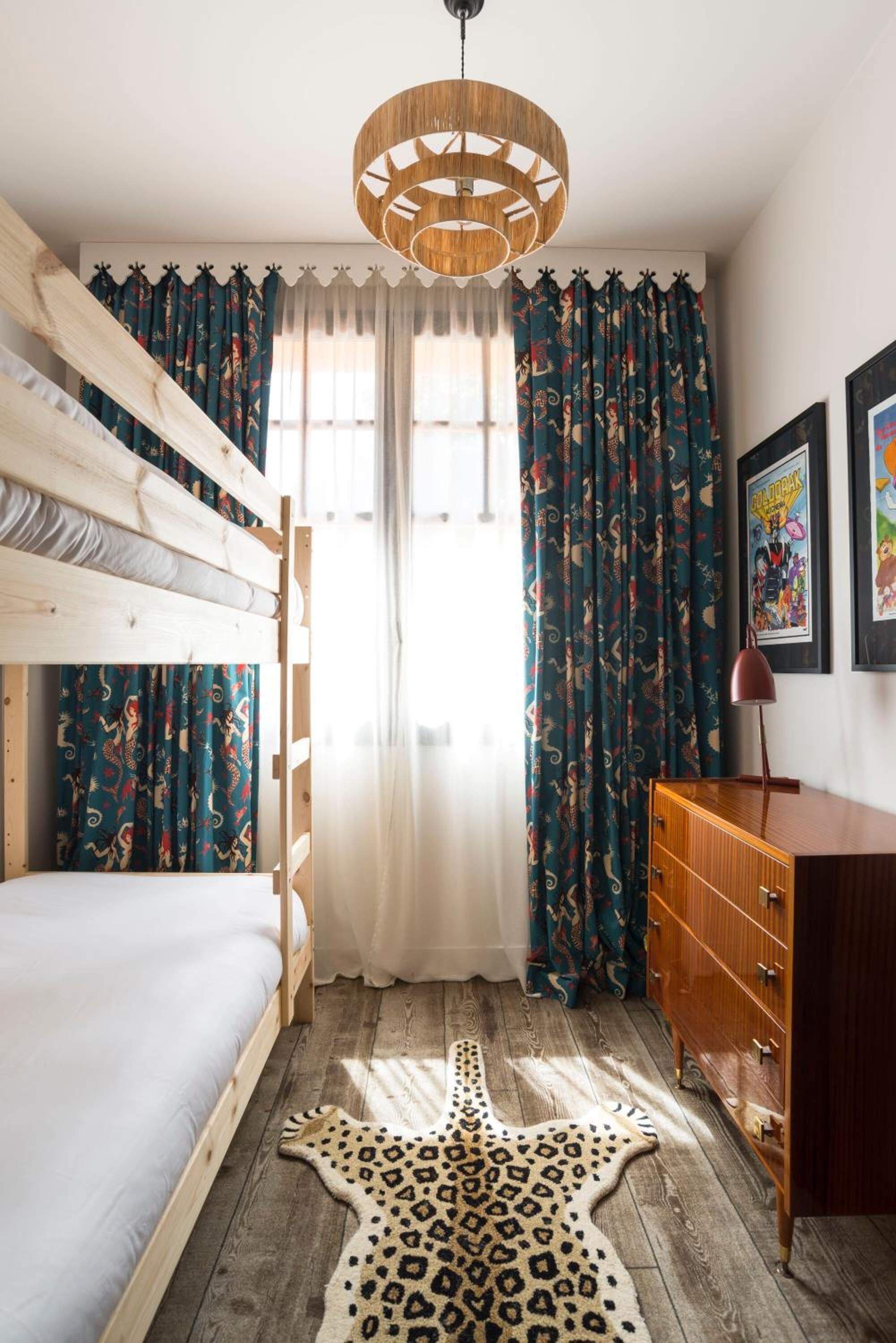 A bedroom with a bunk bed, a wooden dresser, a leopard print rug, and a ceiling light fixture.
