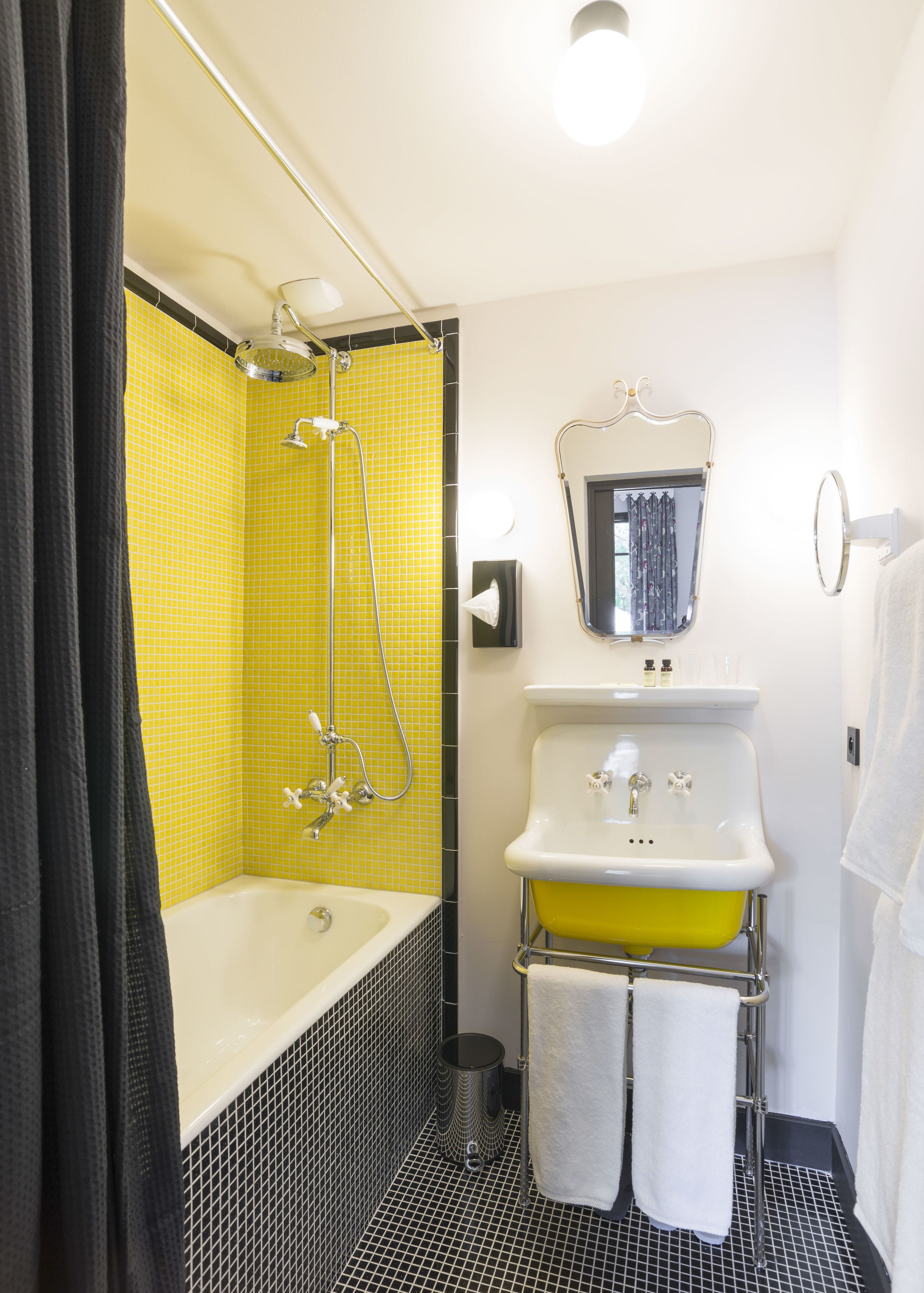 Un bany amb plat de dutxa revestit de rajoles grogues, un lavabo blanc amb rentapel amb tonalitat groga i un mirall sobre el lavabo.