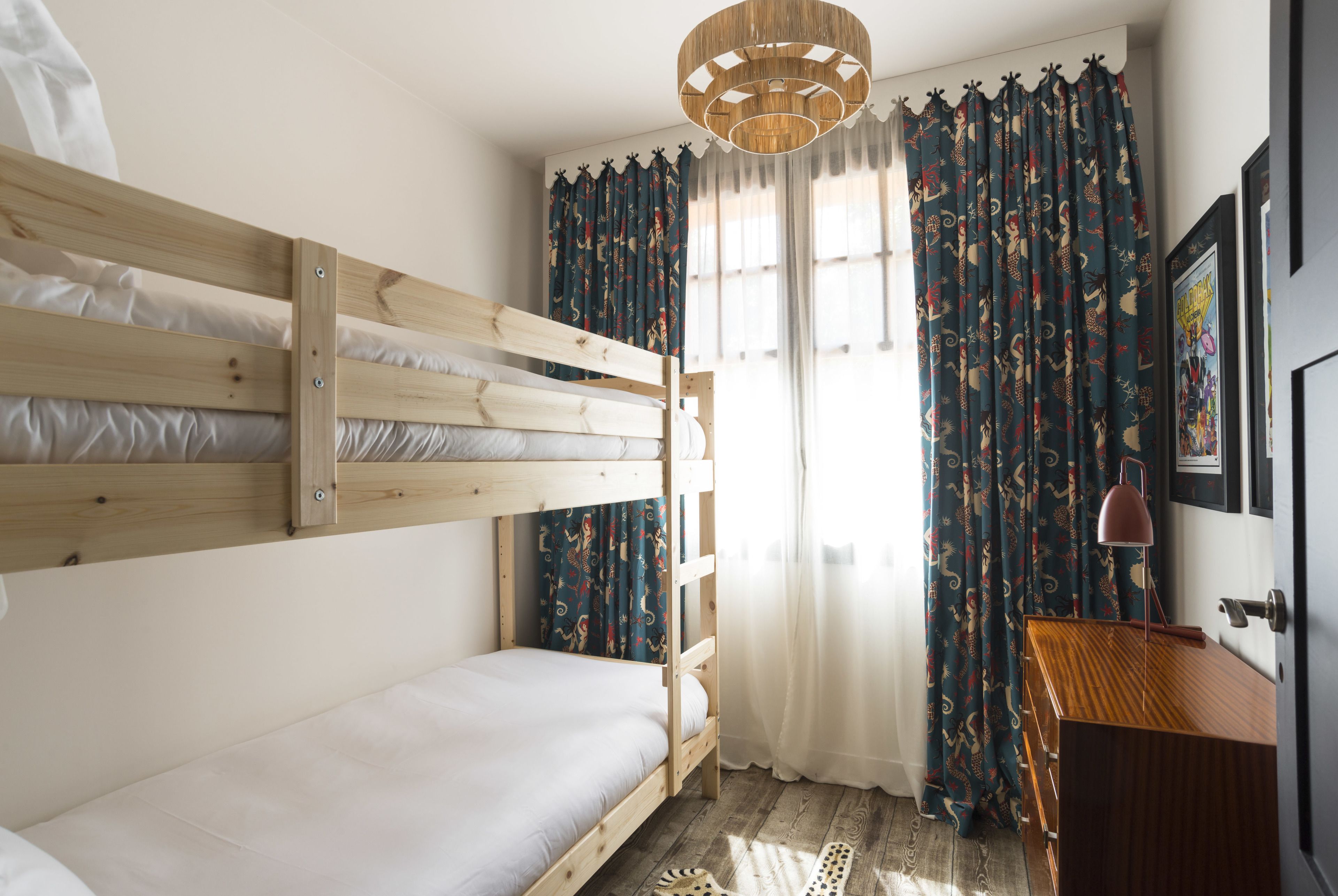 Dormitorio con literas, cabecera de madera, escritorio con lámpara y ventana con cortinas.