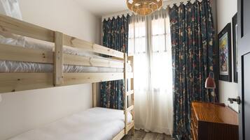 Dormitorio con literas, cabecera de madera, escritorio con lámpara y ventana con cortinas.