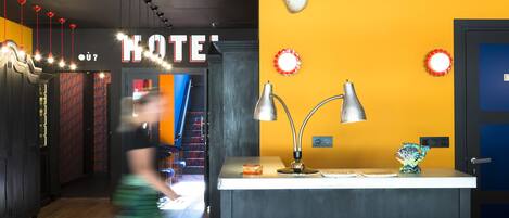 A hotel lobby with a reception desk, a 'HOTEL' sign, a 'Bienvenue a nos amis' sign, and a modern interior design.