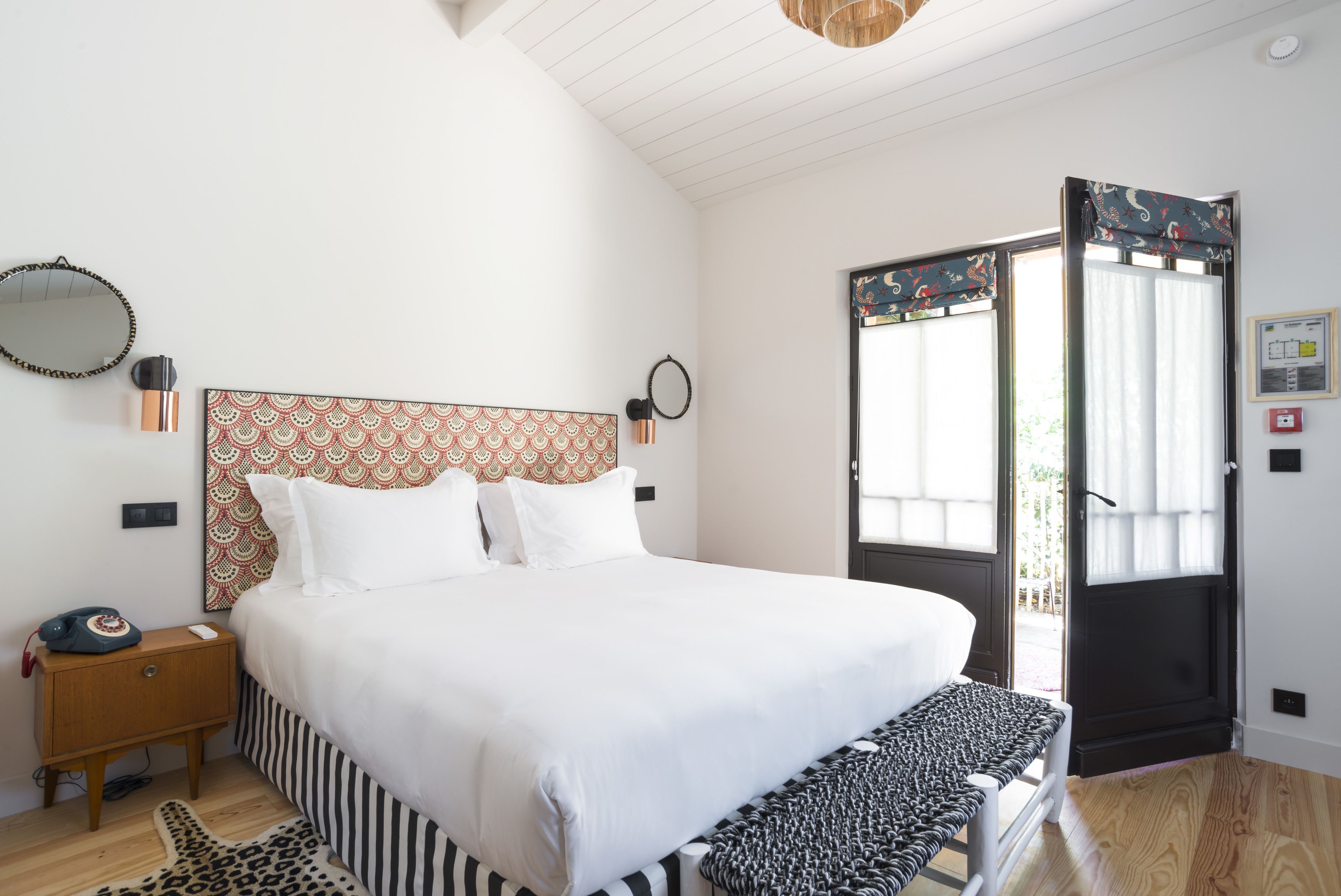 Un dormitorio ordenado con una cama grande, mesitas de noche, un cabecero estampado y un banco al pie de la cama.
